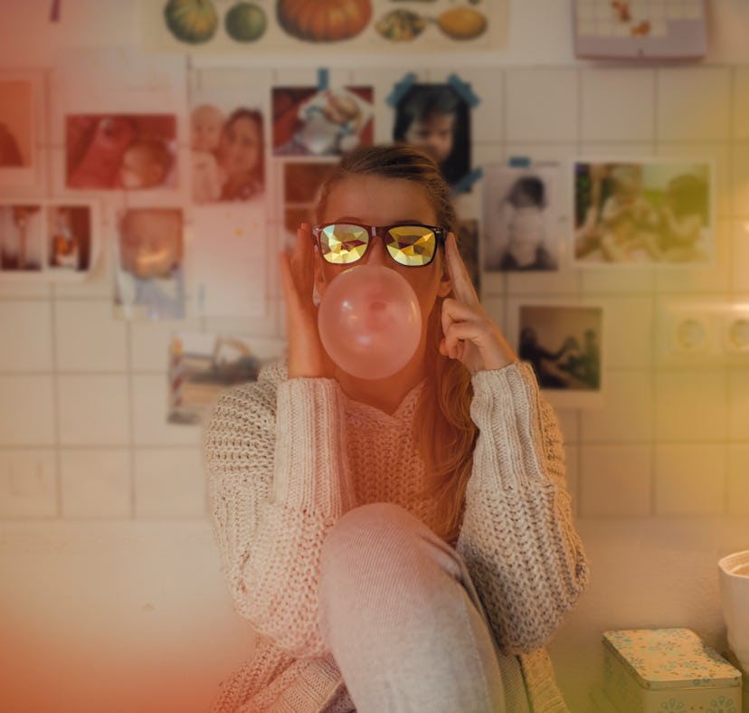 Young woman wearing sunglasses, blowing a bubble before posting a pic on Instagram with a sweet gum,...