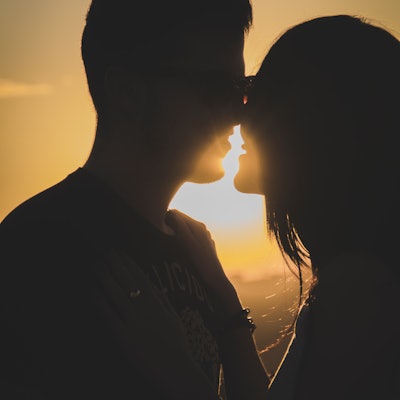 A silhouette of two people kissing with the sun in the background.