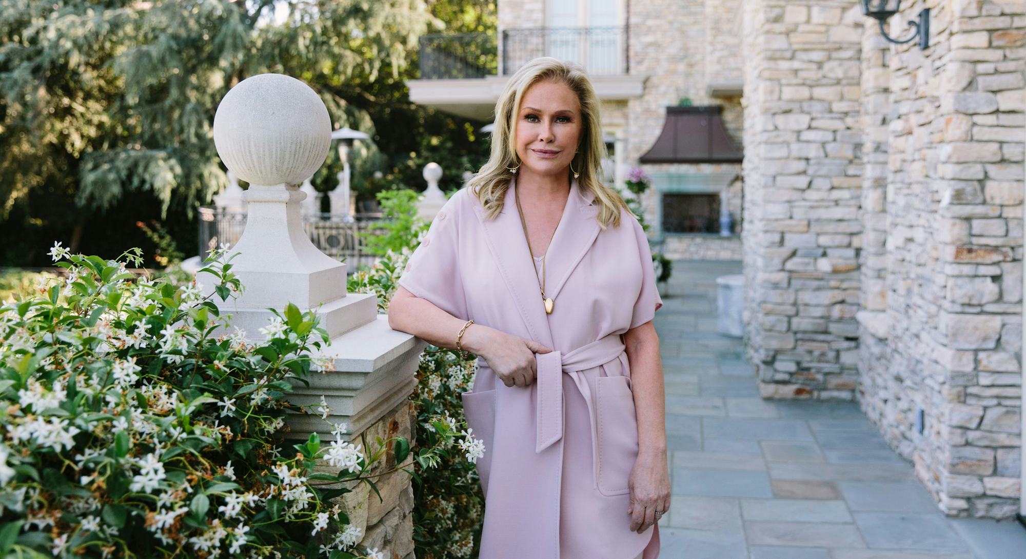 Kathy Hilton stands near a garden as she poses for Bustle.