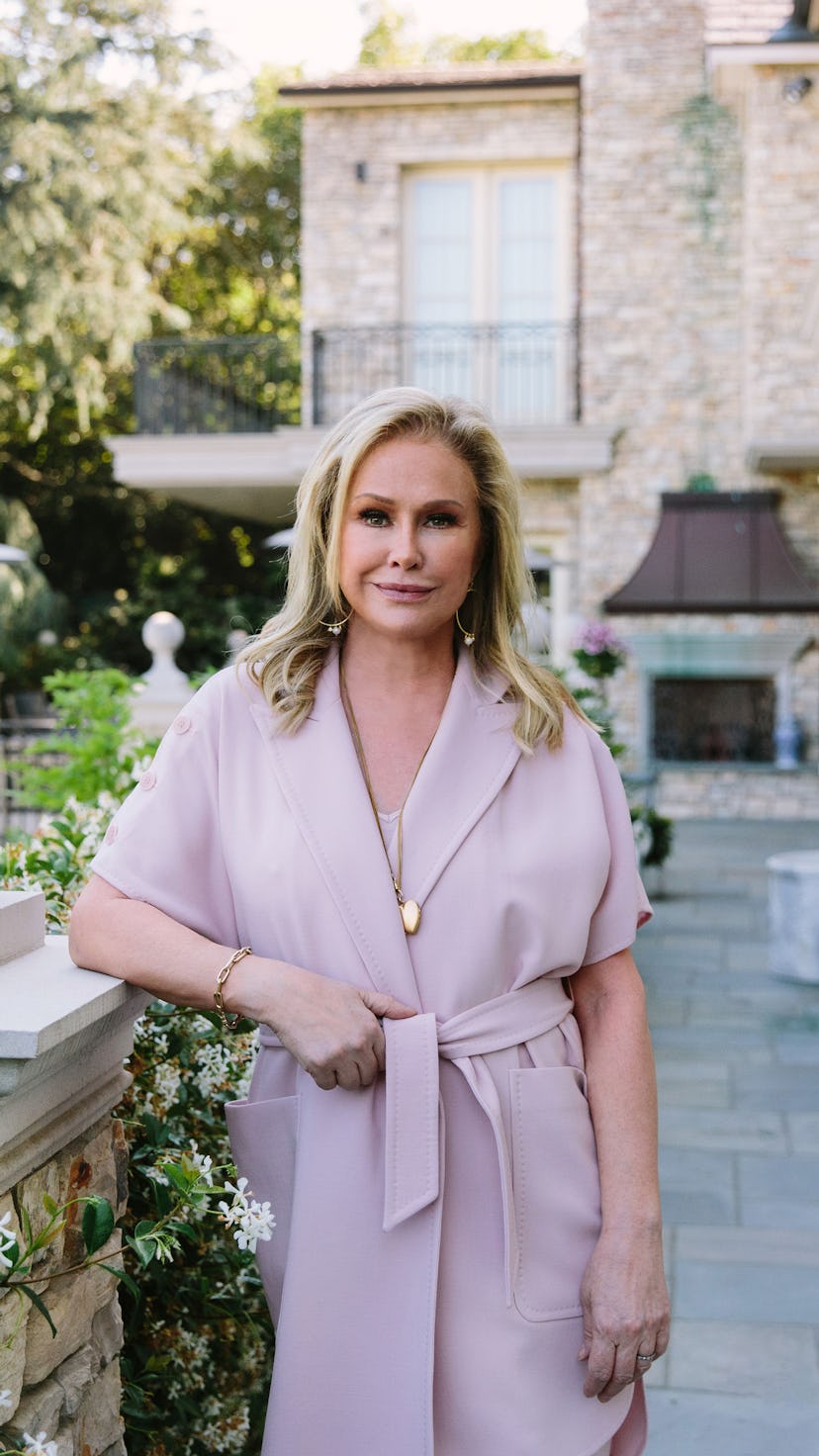 Kathy Hilton stands near a garden as she poses for Bustle.