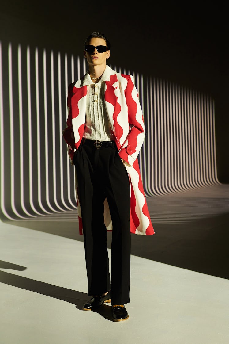 A model in a beige top, beige-red coat, and black trousers by Casablanca at Men’s Fashion Week Sprin...