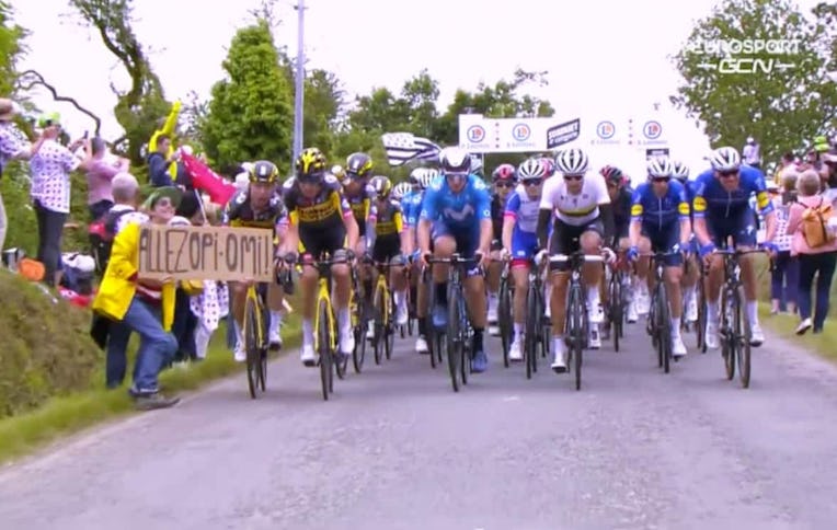 Tour de France cyclists on the road, with a spectator on the side holding a sign into the road.