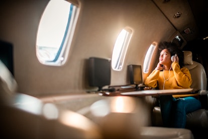 Young woman staring out plane window on the best day for her to travel in fall 2021, per her zodiac ...