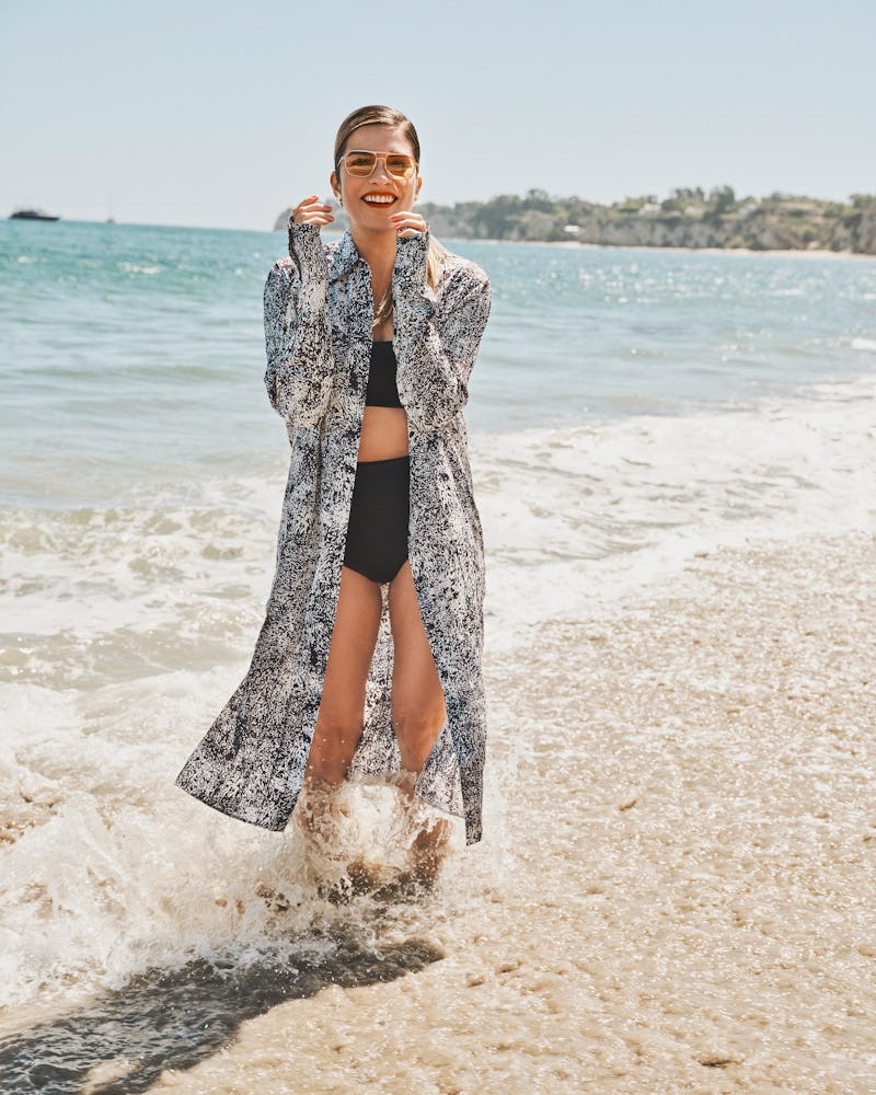 Annie Murphy, star of 'Schitt's Creek' & 'Kevin Can F*ck Himself,' stands on a beach near water wear...