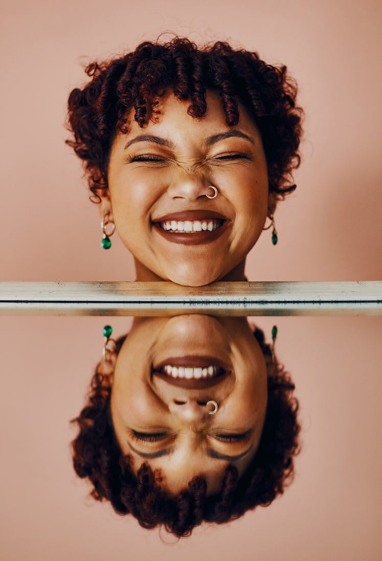 Young woman smiling next to her reflection because of her best July 2021 monthly horoscope.