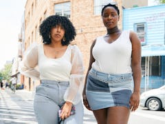 Two plus-size Black women standing on a street corner wearing plus-size white tops and denim bottoms...