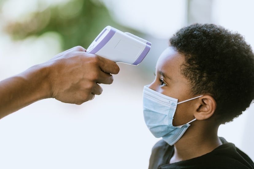 masked child getting his temperature taken at school