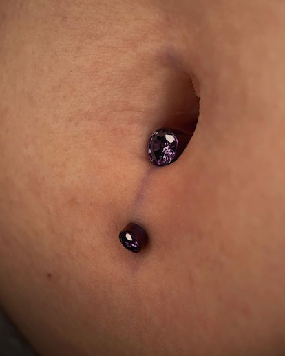 A lower navel piercing with a purple gem/