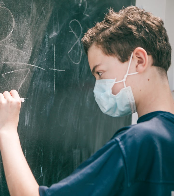 masked student in classroom working out math equations on chalkboard