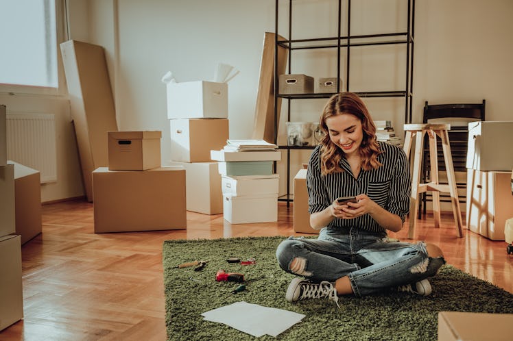 Young woman surrounded by boxes in her new home, ready to post a pic on Instagram with a fun caption...