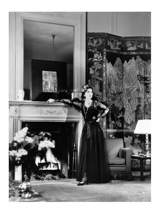 Gabrielle “Coco” Chanel in 1937 posing next to a fire place