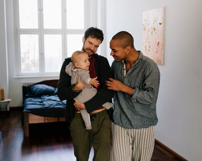 Gay fathers leaving bedroom together carrying newborn son