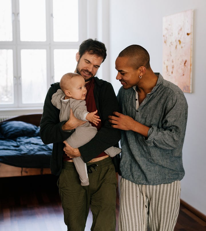 Gay fathers leaving bedroom together carrying newborn son