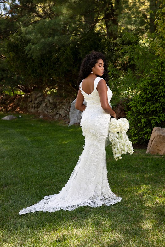 A woman posing in a Christian Siriano bridal dress and holding white flowers
