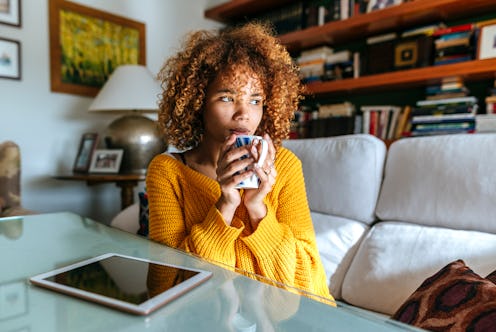 A woman has coffee while sitting in her living room. Experts explain symptoms of caffeine sensitivit...