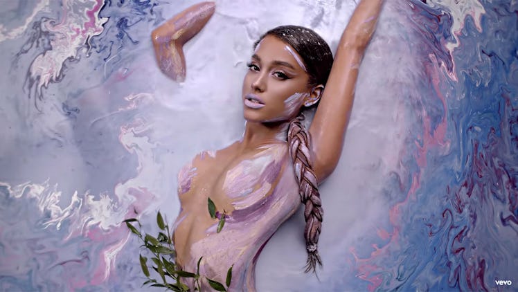 Ariana Grande lying in a pool of multi-colored water with body paint for her "God Is A Woman" music ...
