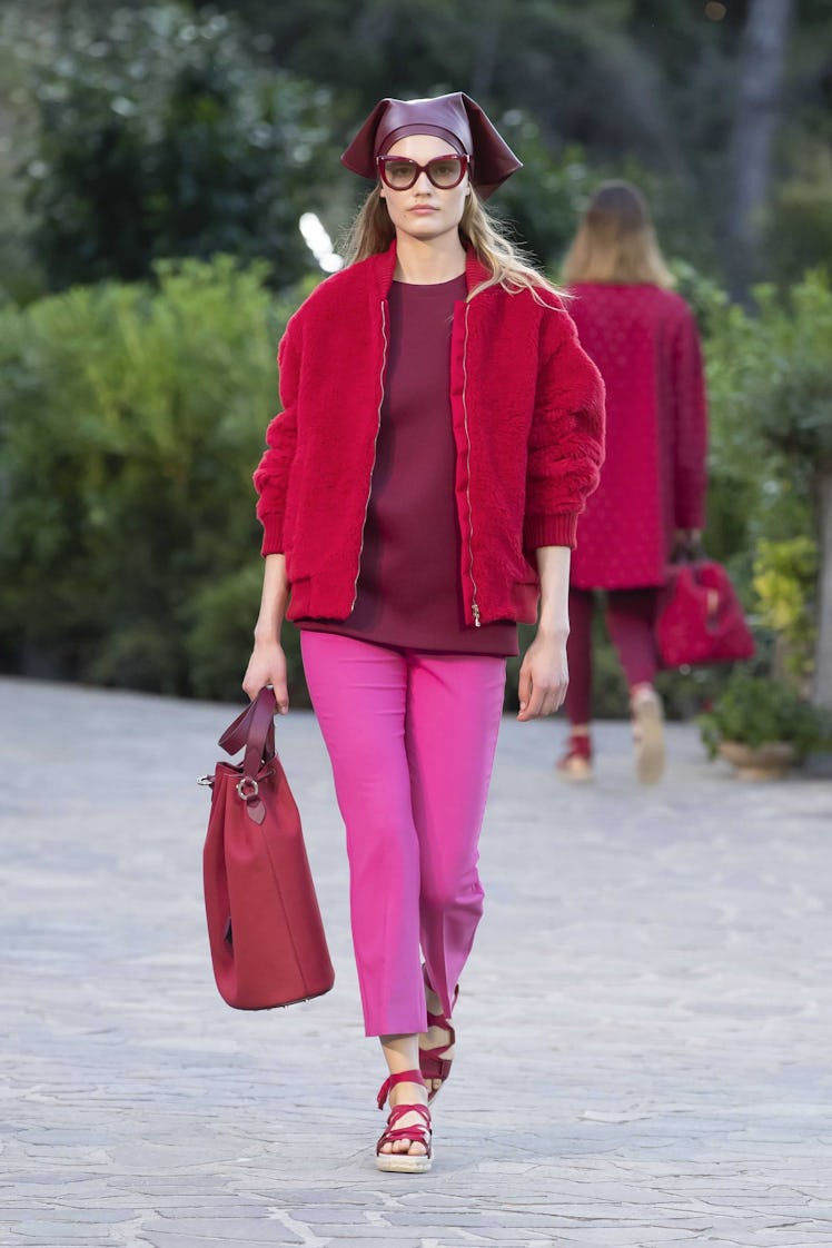 A female model walking while wearing a Max Mara outfit consisted of a red bomber coat, pink pants, a...