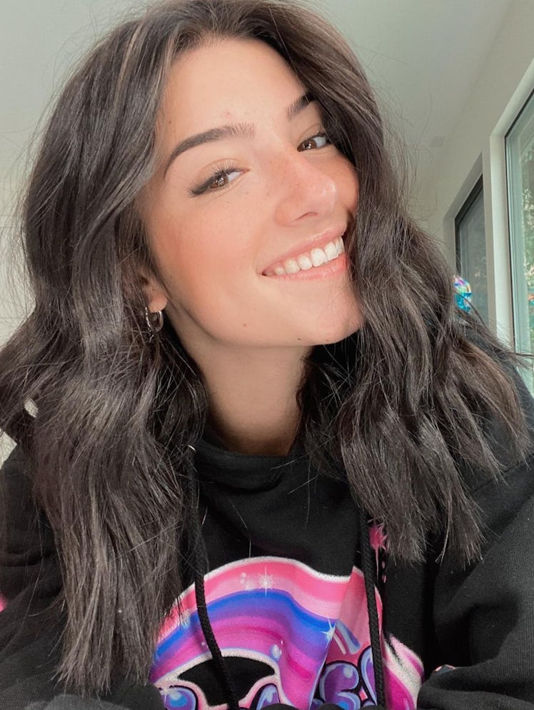 Charli D'Amelio smiles while wearing a black hoodie from her hoodie collection