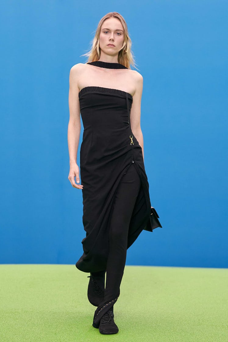 A model walking the runway for Jacquemus in a black dress and boots 