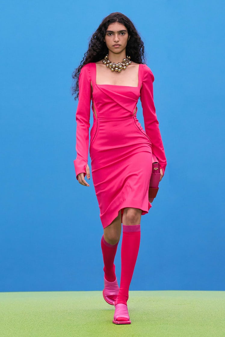 A model walking the runway in a Jacquemus pink dress with matching knee-high boots 
