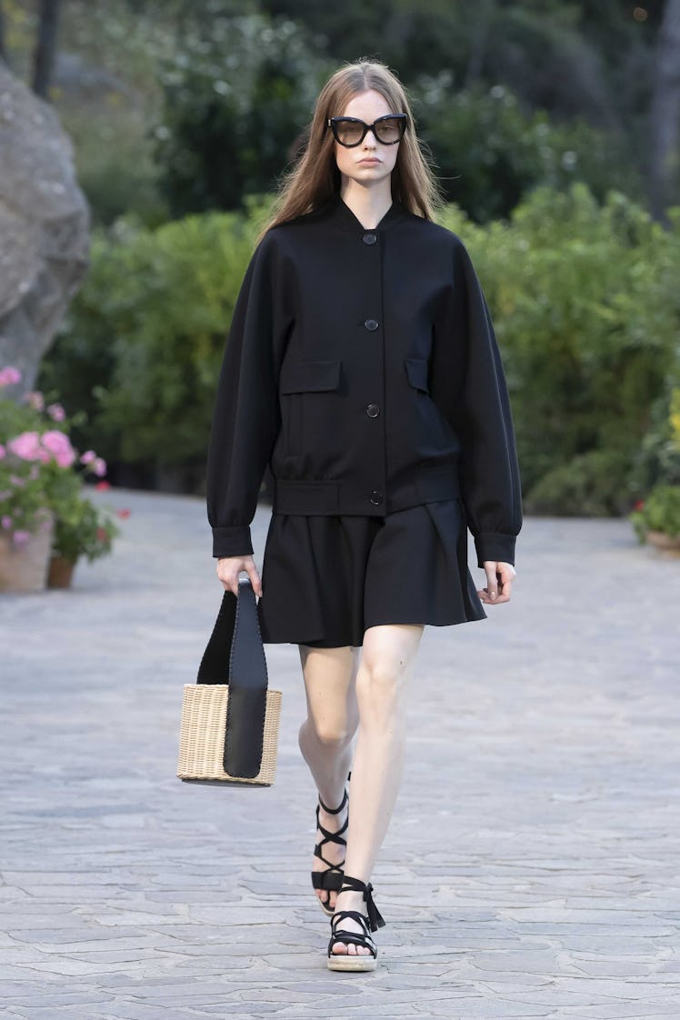 A model walking while wearing a black Max Mara bomber coat and a black Max Mara jersey dress