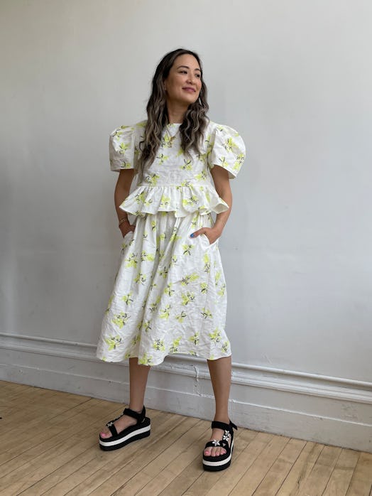 Caroline Maguire in a white-yellow linen floral top and skirt, and layered necklaces that are simple...