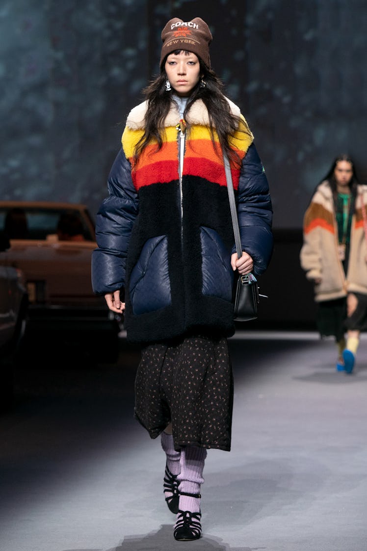A female model walking the Coach Runway while wearing a black, orange, and yellow winter jacket