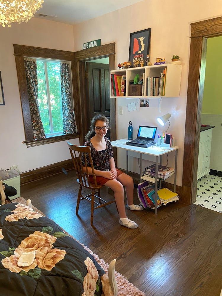  A white girl with her hair in a ponytail is sitting at a desk. There is a computer on top of the de...