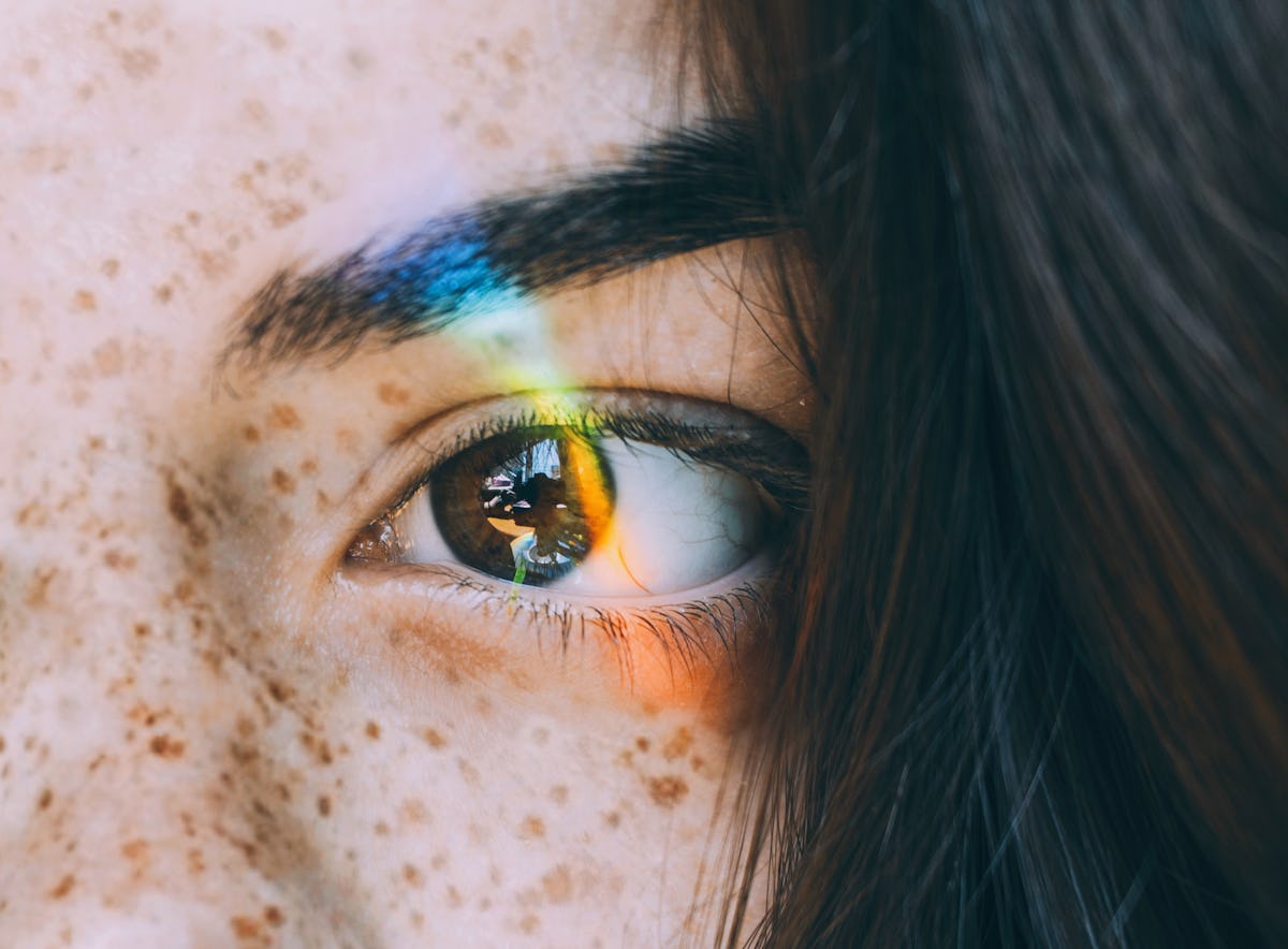 Young woman with rainbow light across eye to show when your dreams will be the most vivid, per your zodiac sign & the moon.