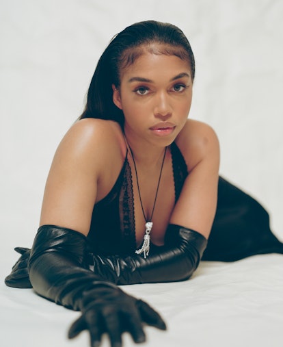 Model Lori Harvey poses on the ground with her hands out in front of her while wearing a black dress...