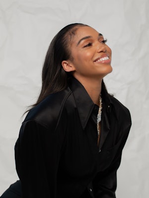 A close-up of Lori Harvey against a white backdrop wearing a black jacket.