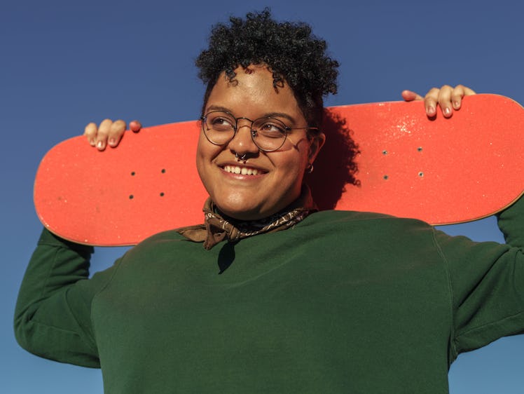 Young person holding skateboard on their shoulders.