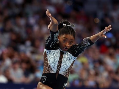 Simone Biles midair with her arms outstretched preparing to go into a roundoff during her floor rout...