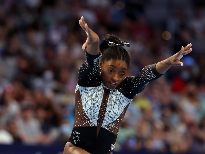 Simone Biles midair with her arms outstretched preparing to go into a roundoff during her floor rout...