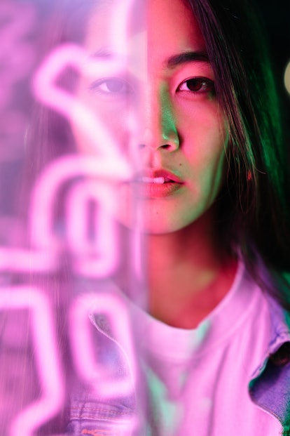 Young woman behind pink neon sign, lights.
