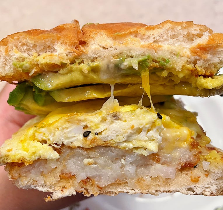 A cross-section of a sandwich with egg, hash brown, cheese, and avocado.