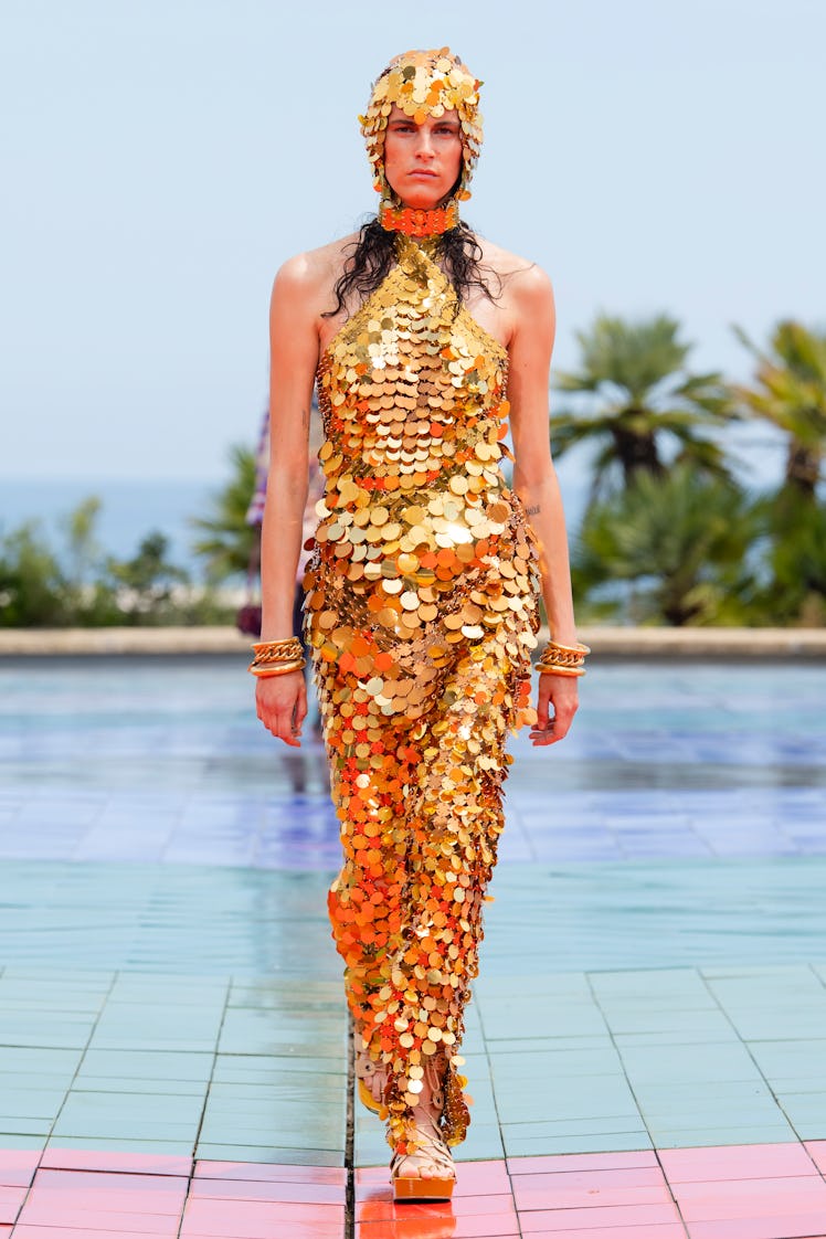 A female model walking while wearing an orange sequined jumpsuit