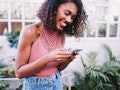 Young woman texting her best friend birthday wishes with plants in the background.