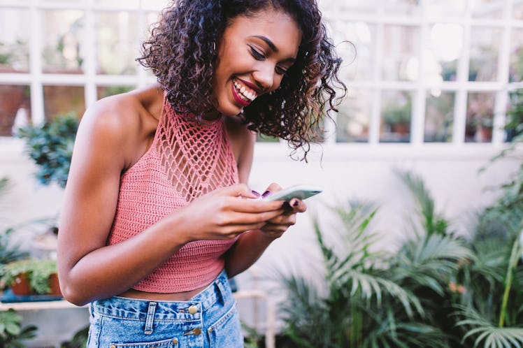 Young woman texting her best friend birthday wishes with plants in the background.