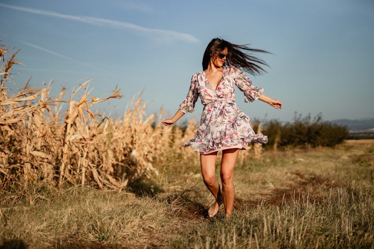 Young woman twirling in a floral summer dress with the wind in her hair before posting a pic on Inst...