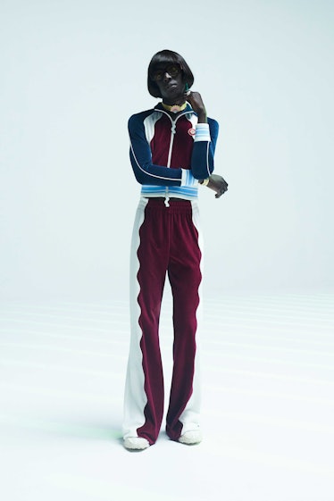 A model posing in a burgundy, white, and blue tracksuit top and pants combination