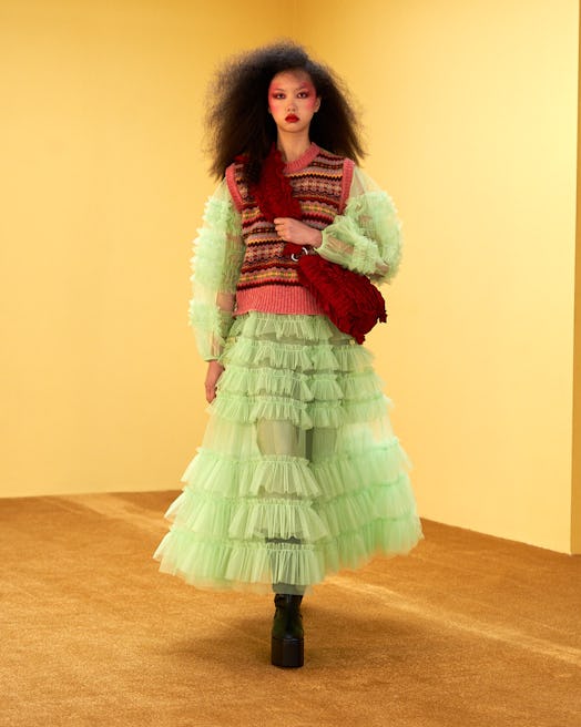 Model wearing a knitted vest over a mint green dress, and a red pouch by Molly Goddard