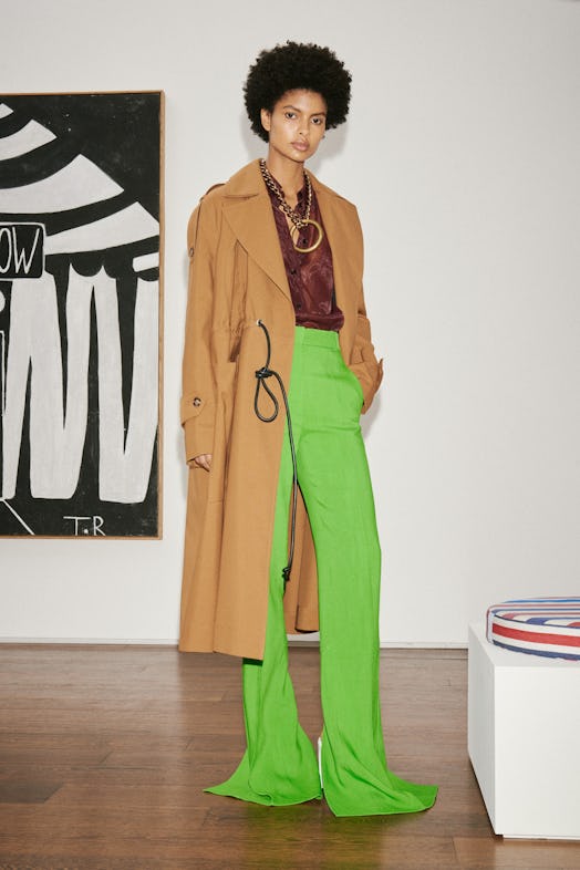 Model wearing a burgundy shirt, brown coat, and bright green pants