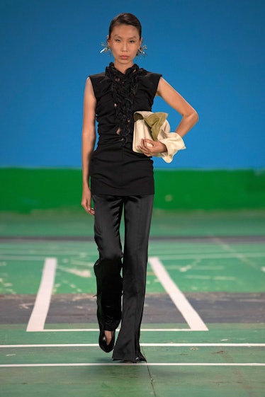 A female model walking while wearing a black sleeveless blouse and black pants