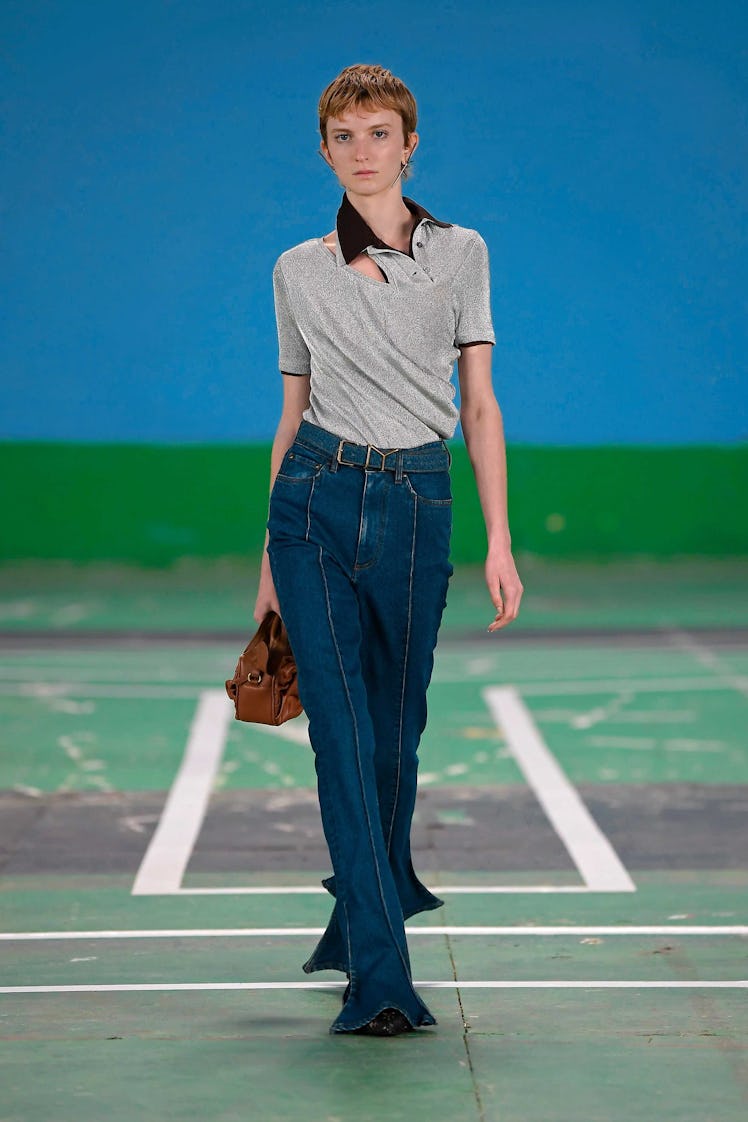 A female model walking while wearing a grey shirt and denim pants