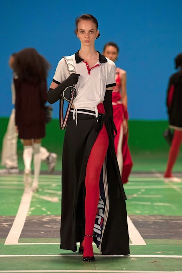 A female model walking while wearing a white and black dress, red leggings, and black long gloves