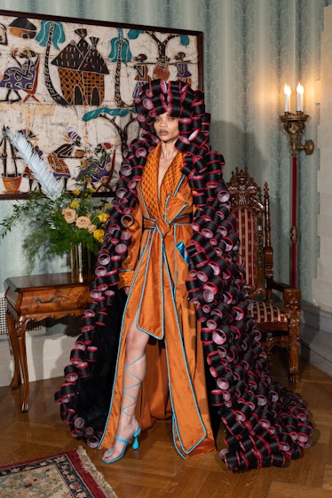A model in an orange Pyer Moss robe and rollers in her hair that goes all the way to the floor 