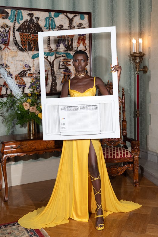 A model in a yellow gown holding a vent from an air conditioning unit.