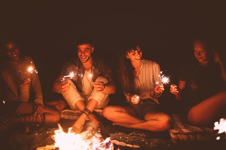 Group of young friends with sparklers around a beach bonfire in need of Instagram captions.