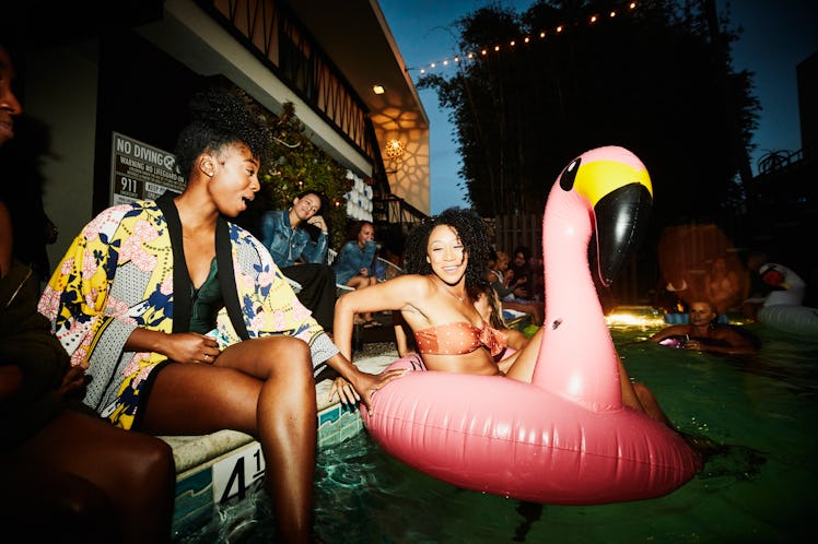 Smiling woman sitting in inflatable flamingo in hotel pool with friends before posting a resort capt...